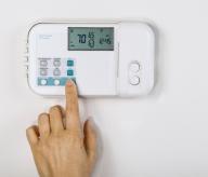 Thermostat on the wall with a hand adjusting the temperature. 