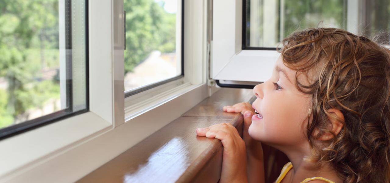 young child looking over the edge of windowsill out open window springtime